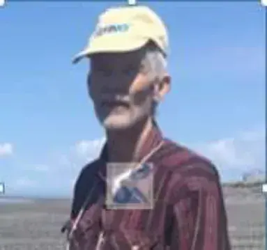 A man with a gray mustache in a cap and plaid shirt outdoors