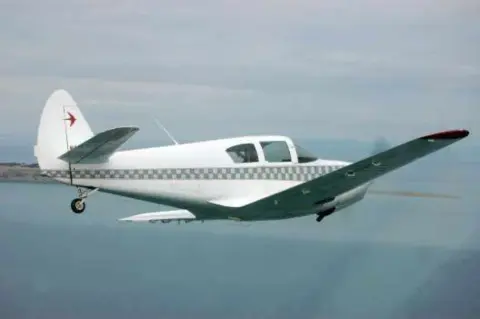 A white low-wing airplane with a red star in flight over water