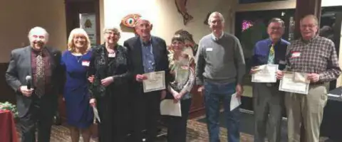 Members holding certificates in a line at the holiday party