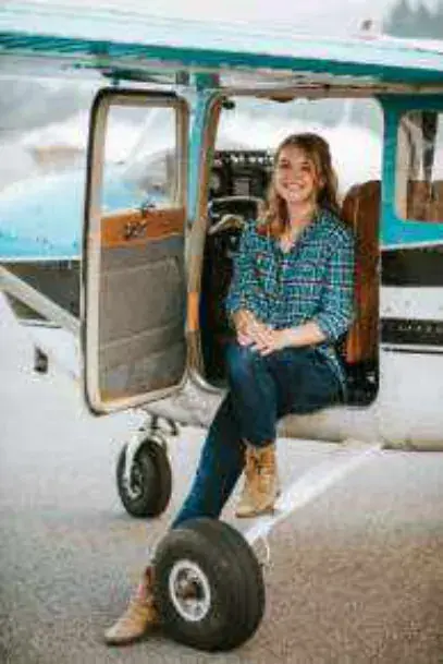 A young woman sitting in the door of a high-wing airplane