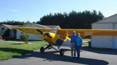 A man and a woman standing beside a yellow Cub-style airplane