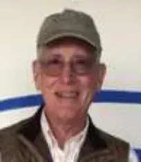 A smiling older man in a green cap and glasses