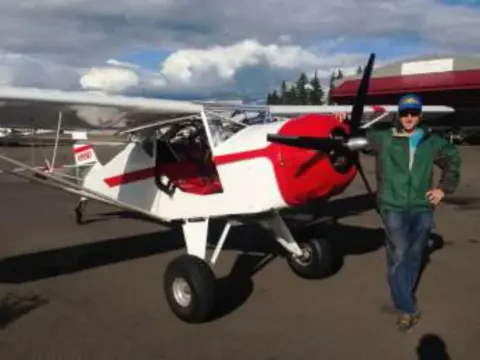 A man beside a red and white backcountry airplane on a gravel ramp