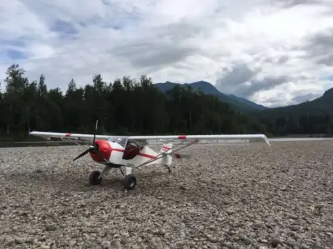 A red and white airplane parked on a gravel strip