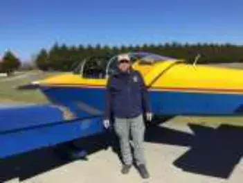 A man standing beside a blue and yellow low-wing airplane on the ramp