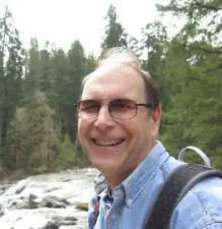 A smiling man with glasses taking a selfie in the woods