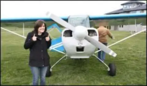 A young woman by the propeller of a white airplane on grass