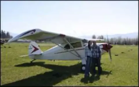 A person standing beside a high-wing airplane on grass
