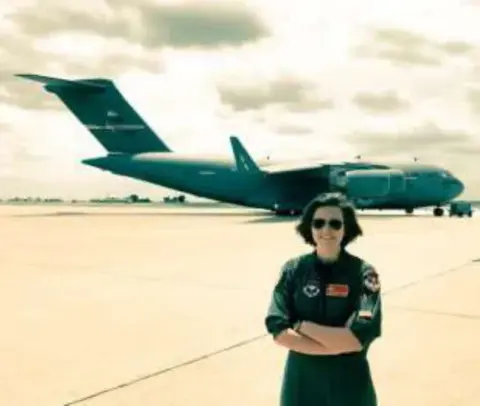 A young woman in a flight suit in front of a military jet transport
