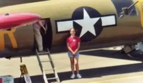 A young woman standing on a ladder at the door of a World War II era airplane