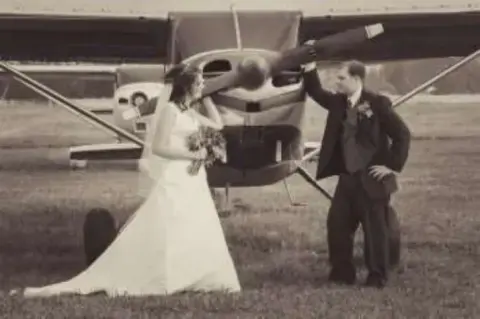 A bride and groom beside the propeller of a small airplane, in black and white