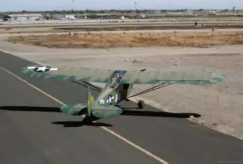 An olive drab Piper Cub with invasion stripes on the runway