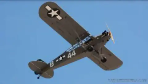 An olive drab Piper Cub numbered 44 in flight