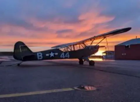 The olive drab Piper Cub numbered 44 at sunset