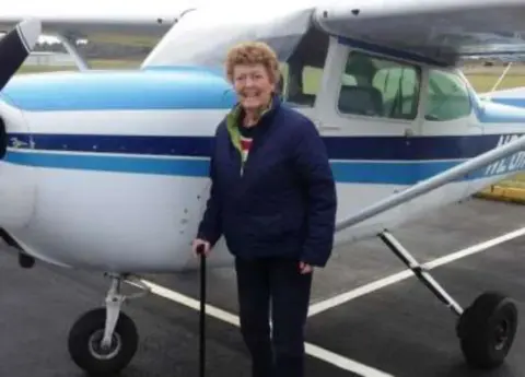 A woman standing by the wing of a blue and white Cessna