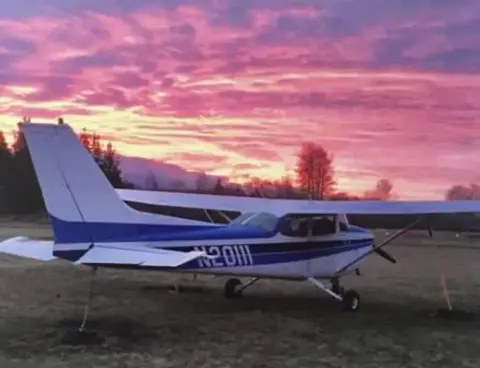 A high-wing airplane parked under a pink sunset sky
