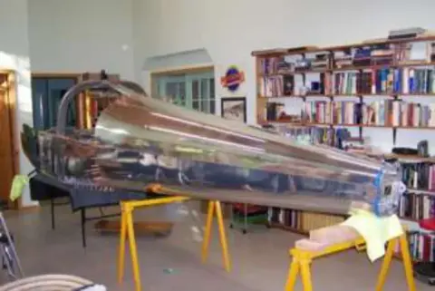 An airplane fuselage on sawhorses in a room with bookshelves