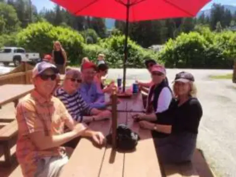 Members having lunch at a picnic table under a red umbrella