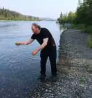 A man skipping a stone at the edge of a river