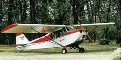 A red and white taildragger parked by trees