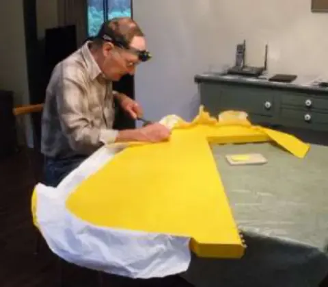 A man working on a yellow control surface at a bench