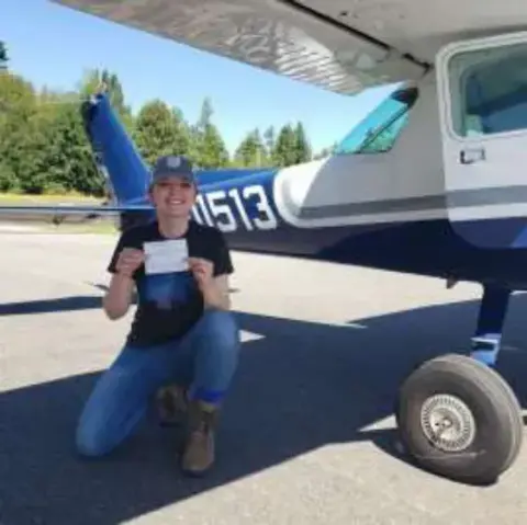 A young man holding a certificate by an airplane