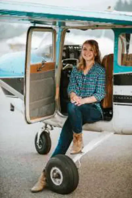 A young woman sitting in the doorway of a high-wing airplane