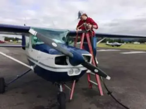 A man on a ladder working on a high-wing airplane on the ramp