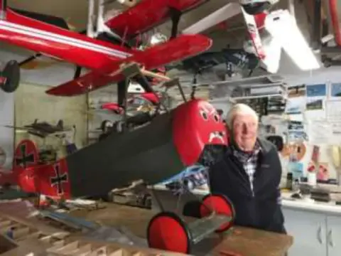 A man in a workshop full of model airplanes