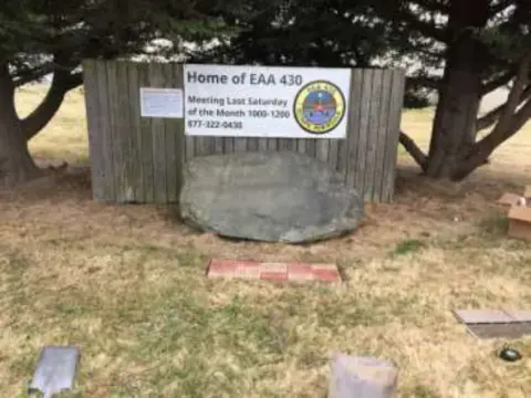 The Home of EAA 430 sign behind a large boulder, with the first pavers set in the grass in front