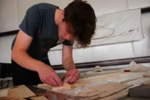 A young man building a balsa model at a table