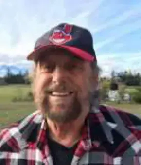 A smiling bearded man in a red cap and plaid shirt outdoors