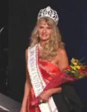 A woman wearing a crown and sash holding flowers