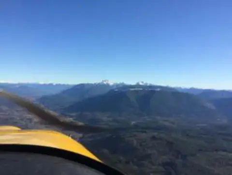 Snowy mountains seen past the wing of a yellow airplane