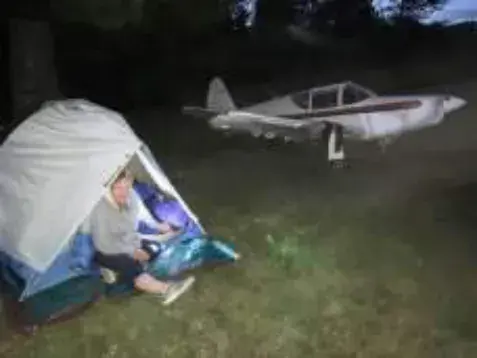 A tent pitched under the wing of a low-wing airplane at night