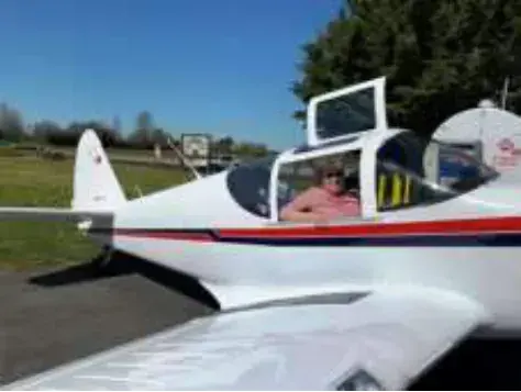 A woman in the cockpit of a red and white low-wing airplane