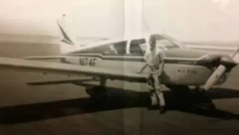 An old photo of a man next to a low-wing airplane