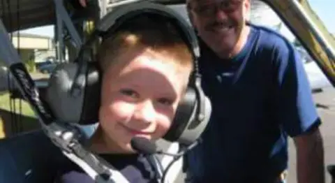 A smiling boy in a headset with a man in the cockpit