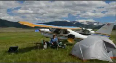 A high-wing airplane on a backcountry strip with a tent pitched beside it
