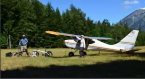 A white high-wing airplane parked in a mountain meadow