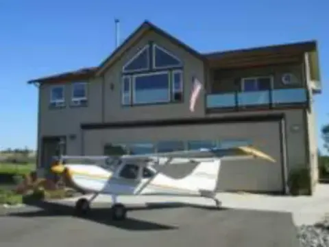 A white high-wing airplane parked in front of a house