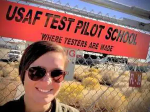 A smiling young woman in front of a USAF Test Pilot School sign