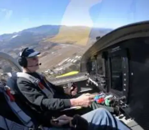 A pilot at the controls in a cockpit over mountains
