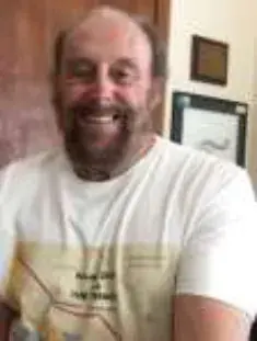 A smiling bald man with a mustache in a white T-shirt indoors
