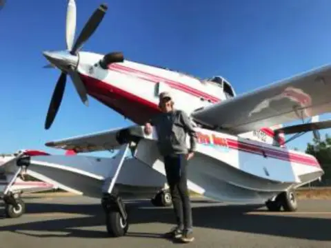 A man standing next to a red and white floatplane in a hangar