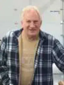 A smiling white-haired man in a plaid shirt