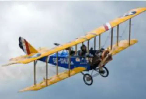 A yellow and blue Jenny biplane in flight