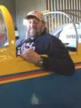 A man in a cap leaning on the cockpit edge of a yellow airplane in a hangar