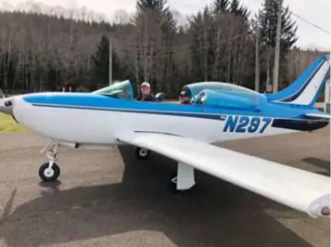 Two people beside a blue and white low-wing airplane, N297, on the ramp