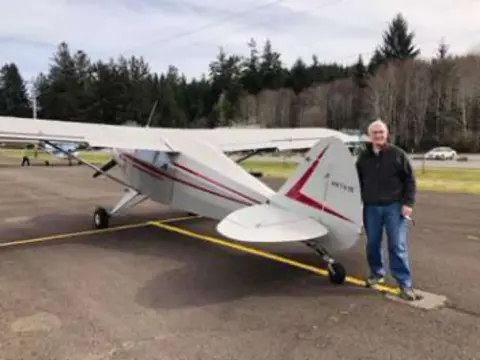 A man standing beside a white high-wing airplane on the ramp